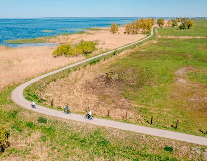 Cyclists on a path along fields and water