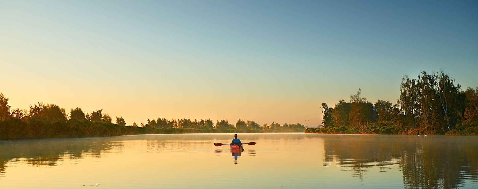 A kayak on the river from behind in tomorrow&#39;s mood. Light fog comes up from the river. The overgrown banks on the sides recognizable