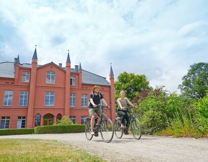 Zwei Fahrradfahrer, die vom Gutshaus Wietzow wegfahren.