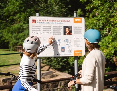 Zwei Personen mit Fahrrad stehen an der Infotafel und die Frau zeigt auf etwas.