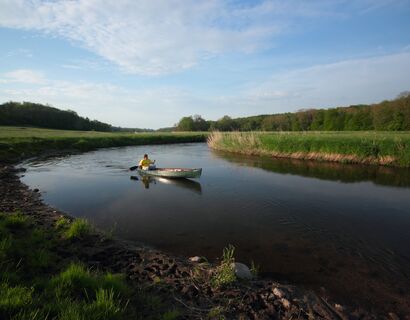 Der Fluss macht eine Knick, auf ihm ein Kanufahrer. begrünte Ufer.