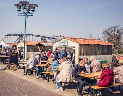 Fischmarkt Wieck Viele Menschen auf Bierbänken und an Tischen am Essen. Neben den alten Bootshütten am Hafen in Wieck