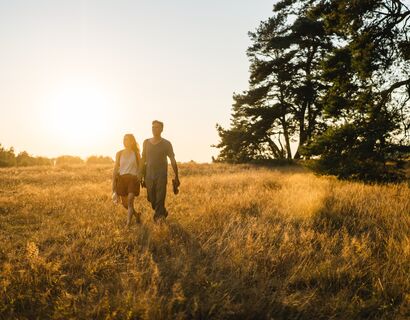 Paar spaziert im Sonnenuntergang über eine Wiese mit hohem Gras.