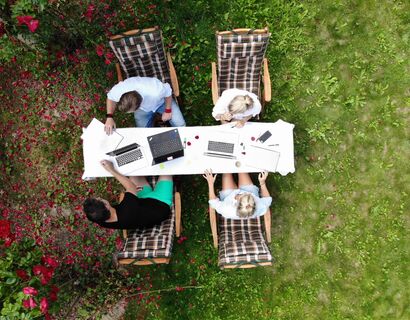 Vier Personen sitzen am Laptop arbeitend im Garten.