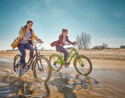 Two cyclists driving through the water on the beach