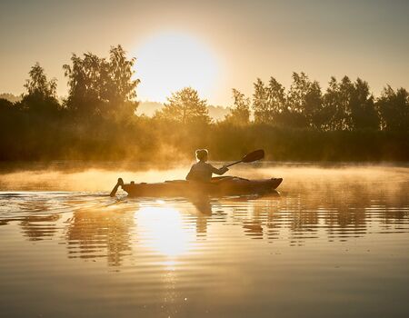 Ein Kajak auf dem Fluss von der Seite in Morgen Stimmung. Nebel kommt vom Fluss hoch.