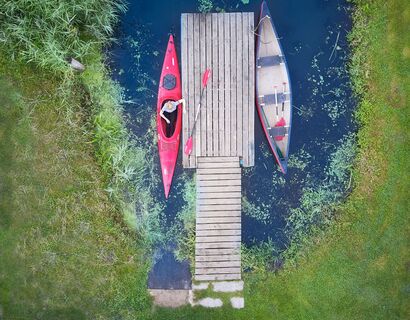 Recording from a bird&#39;s eye view. Central to a jetty with a canoe on the left and right. Someone sits in the left. Below in the picture there are 8 more canoes in red and green.