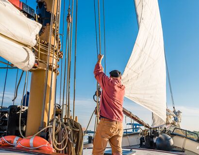 A man on a boat pulling up the sail.