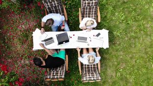 Vier Personen sitzen am Laptop arbeitend im Garten.