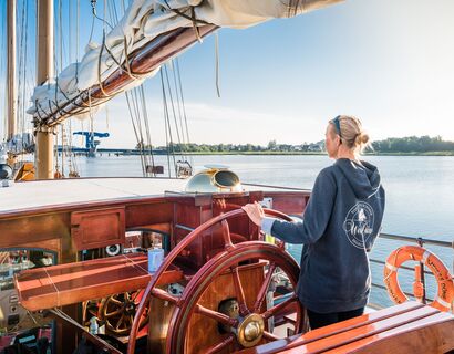 A woman at the wheel of a sailboat.