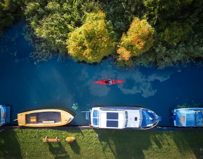 Recording from a bird&#39;s eye view, from left to right you can see a river with different boats on the lower pier, on the river there is a canoe and the forest is forest