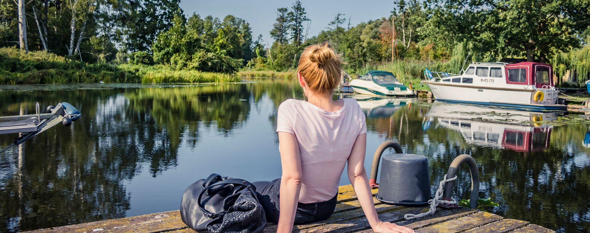 A woman with a backpack next to her sits on a jetty on the water