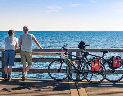 Auf dem Ostseeküstenradweg zum Ostseebad Boltenhagen Zwei Männer stehen auf einem Steg und blicken aufs Meer. Ans Geländer angelehnt stehen neben ihnen ihre Fahrräder.