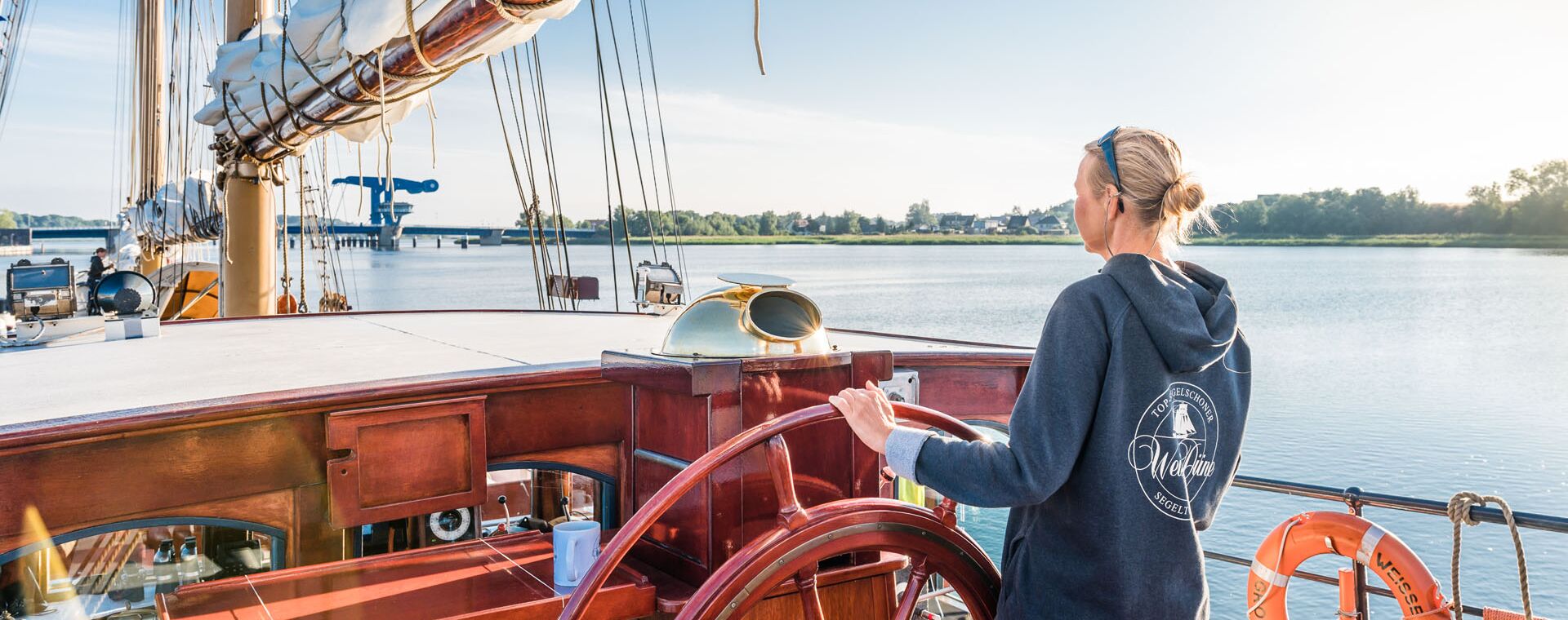 A woman at the wheel of a sailboat.