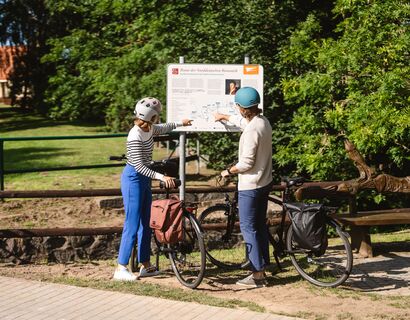 Two people by bike are on the information board and point to something.