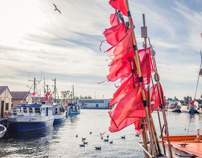 Rote Fahnen, dahinter der Hafen von Freest. Ein paar Möwen schwimmen auf dem Wasser