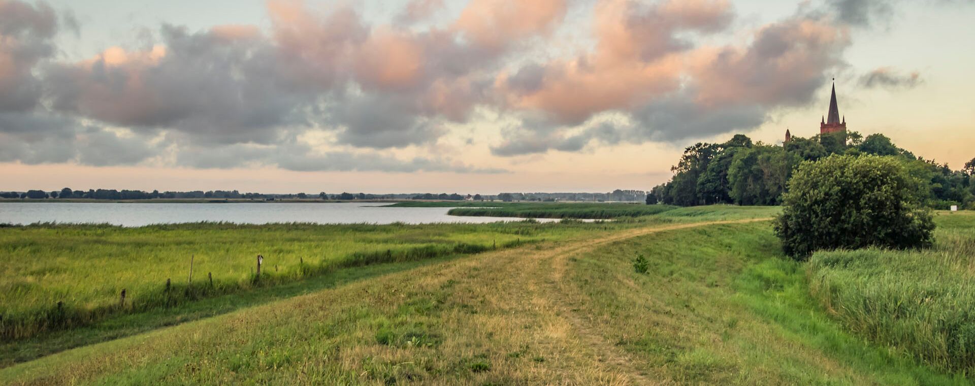 Evening mood on a path on the water with a view of the top of the church from the church in Gristow