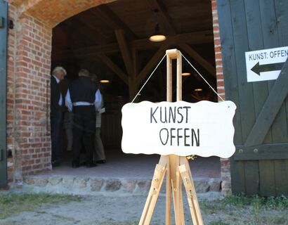 Ein Schild,  auf dem "KUNST OFFEN" steht, vor einer Scheune.