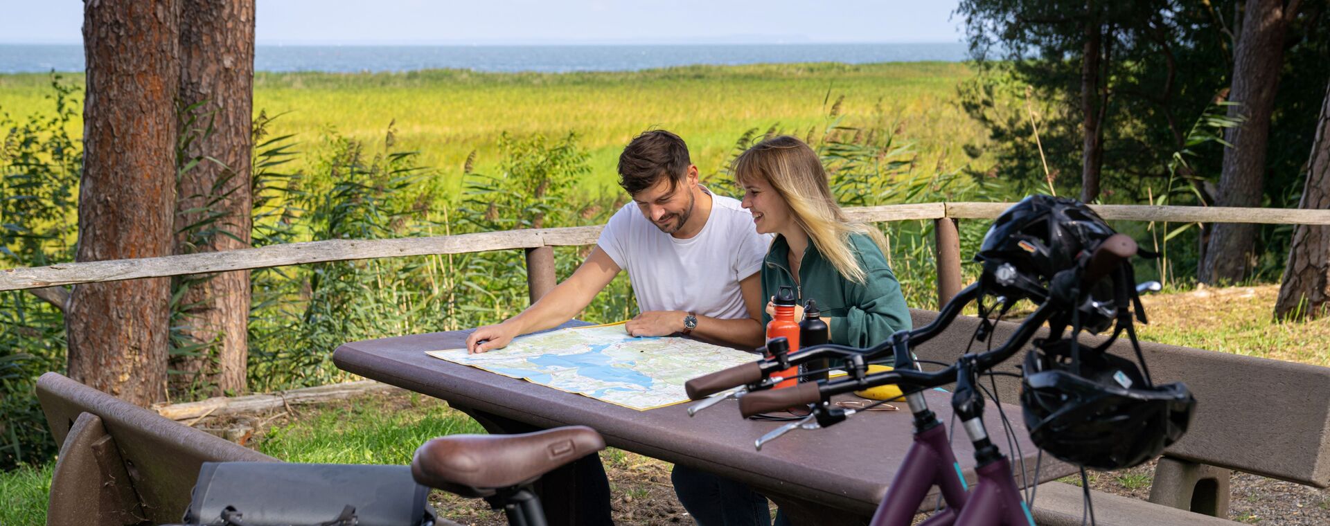 Couple sits at the table from a resting palatinate and look at a card. In the foreground bicycles, the lagoon in the background.