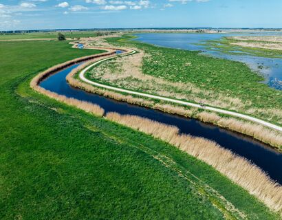 Ein Radweg, der sich an einem Fluss lang schlängelt und auch auf der anderen Seite von Wasser umgeben ist