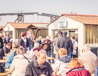 Menschen auf Bierbänken beim Fischerfest in Wieck. Im Hintergrund ein Bratfischstand.