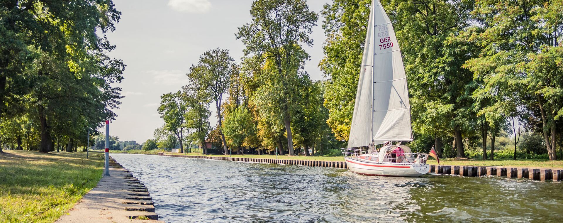 Entry towards the port of a sailboat. Trees and the bank edge are attached to the left and right.