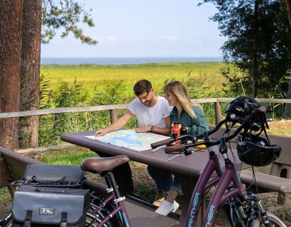 Couple sits at the table from a resting palatinate and look at a card. In the foreground bicycles, the lagoon in the background.