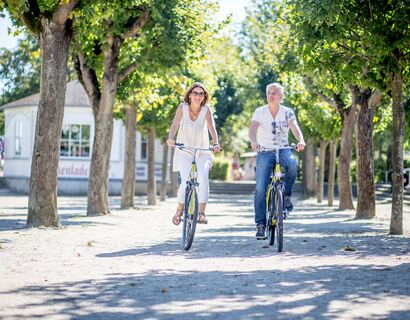 Pärchenurlaub im Ostseebad Heringsdorf Ein Paar fährt auf Fahrrädern durch eine Allee auf die Kamera zu. Die Sonne scheint in Heringsdorgf