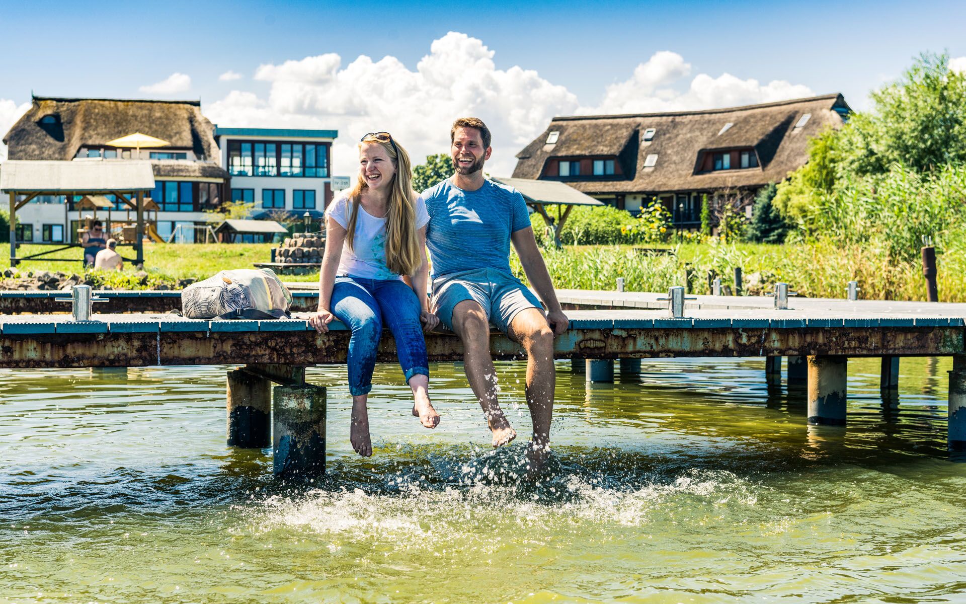 A couple sits on the jetty in front of the Haffhus and lets the legs dangle into the water.