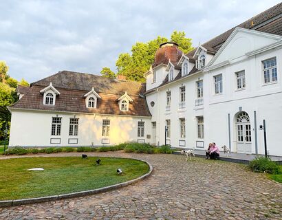 Till Richter und Frau sitzen vor dem Schloss Buggenhagen und zwei Dalmatiner laufen herum